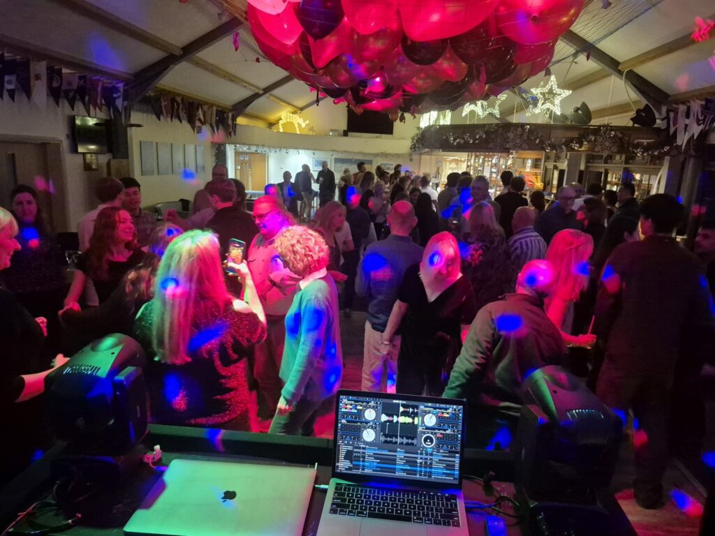A packed dance floor seen from behind the DJ decks