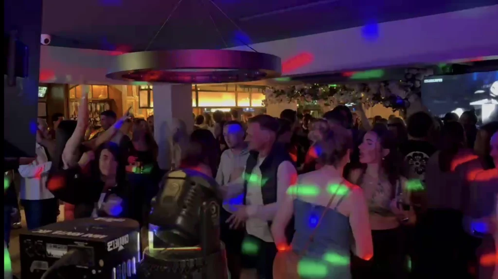 A packed bar dance floor under coloured party lights